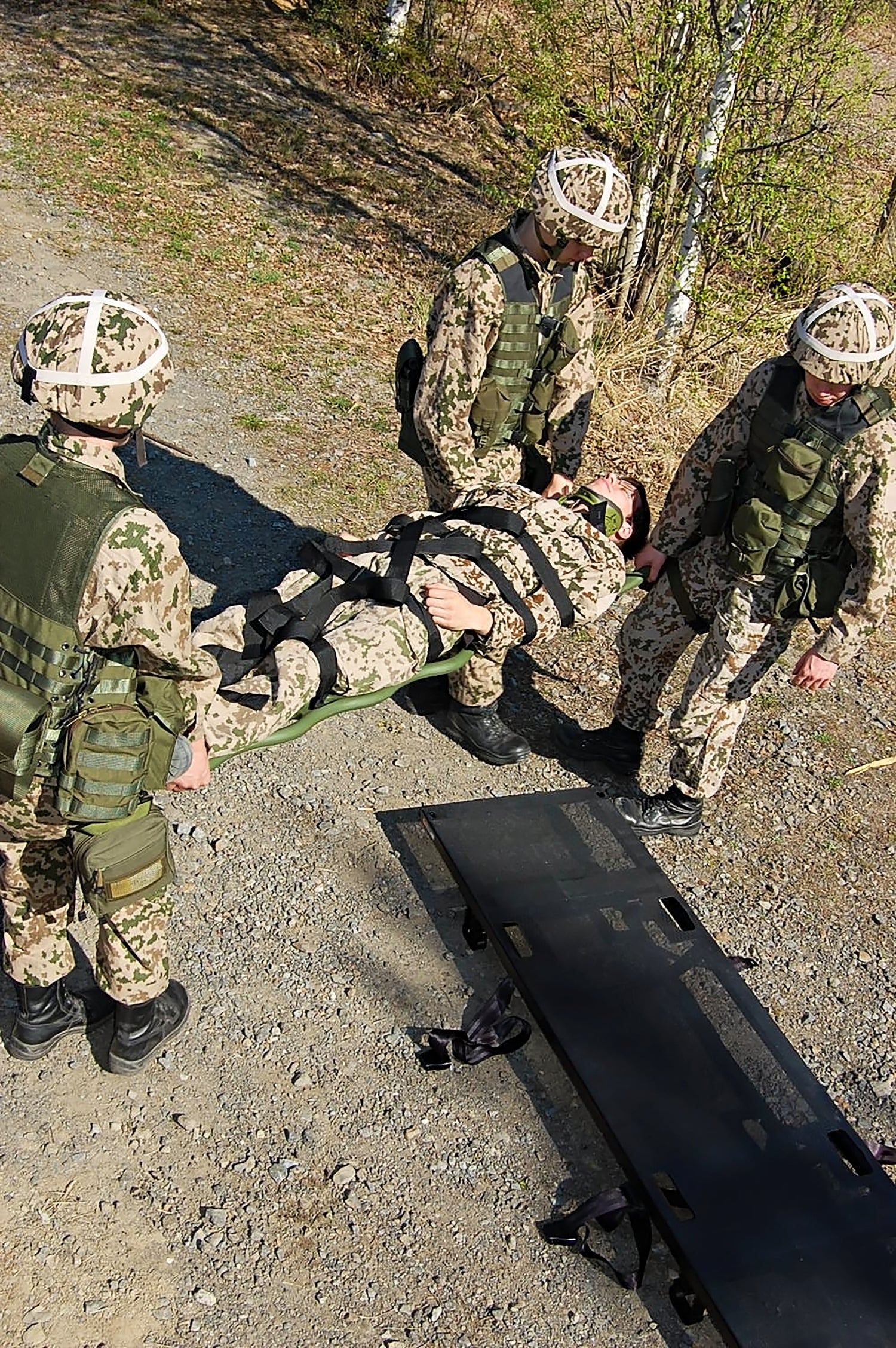 Military medics evacuating a casualty on spinal board onto ProMIL 217 NATO field stretcher